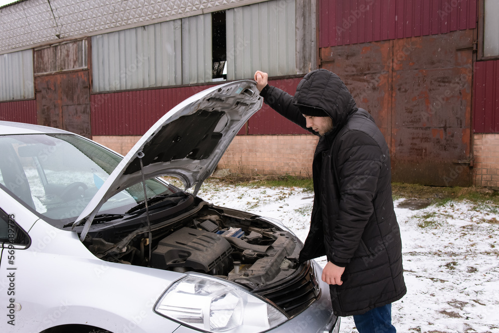 Car repair.Opened hood.Car details.Automobile theme.Repair shop.Gray auto.Auto standing in the street in winter.Car breakdown.Automotive.The man opened the hood.He is looking for a problem in the car.