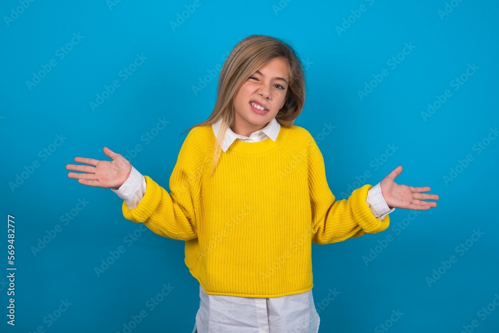 Clueless caucasian teen girl wearing yellow sweater over blue studio background shrugs shoulders with hesitation, faces doubtful situation, spreads palms, Hard decision Clueless caucasian teen girl wearing yellow sweater over blue studio background shrugs shoulders with hesitation, faces doubtful situation, spreads palms, Hard decision