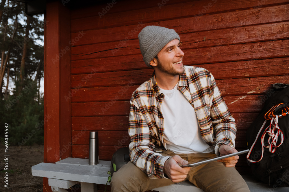 Cheerful man using tablet while sitting on bench in forest Cheerful man using tablet while sitting on bench in forest