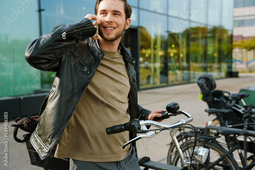 Young man talking on cellphone while standing with bicycle outside