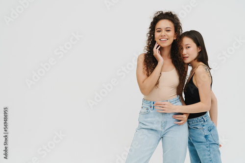 Two young multinational girls posing isolated over white wall