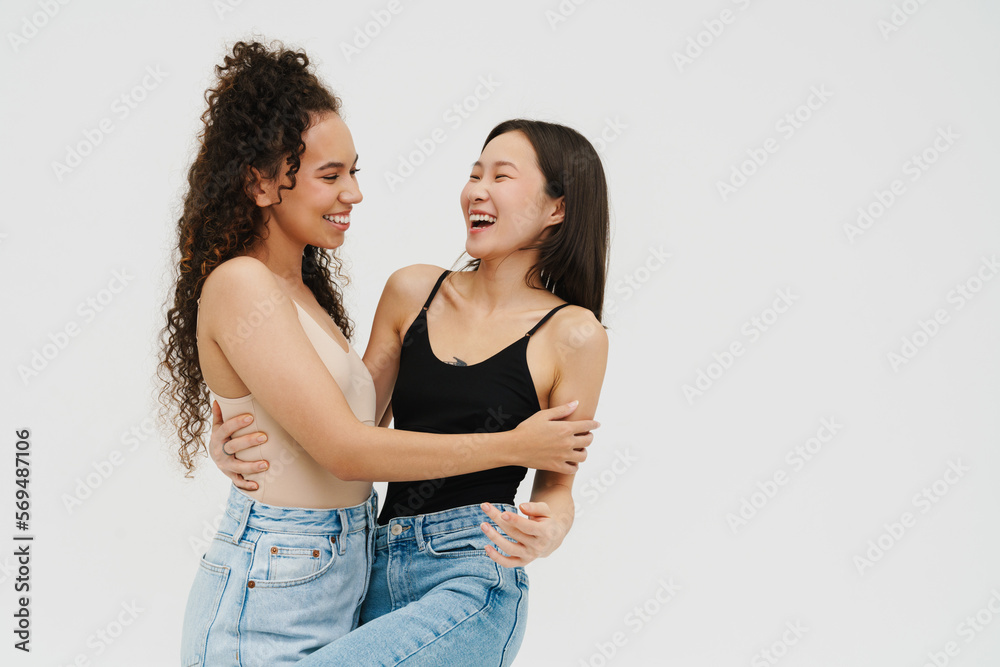Two pretty girls smiling at each other while posing isolated over white wall Two pretty girls smiling at each other while posing isolated over white wall