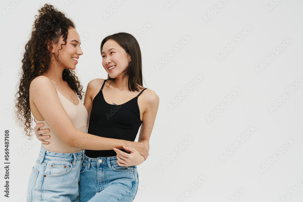 Beautiful multinational girls smiling and hugging while standing over isolated white background Beautiful multinational girls smiling and hugging while standing over isolated white background