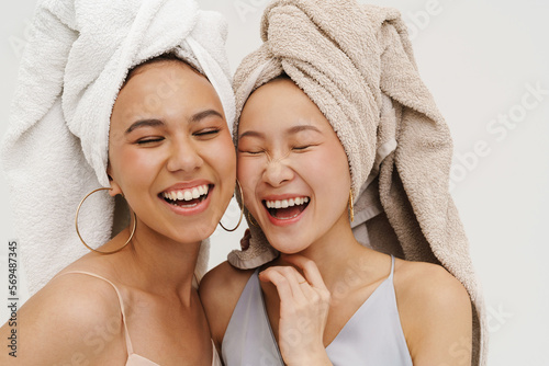 Two cheerful women wearing bath towels laughing while posing isolated