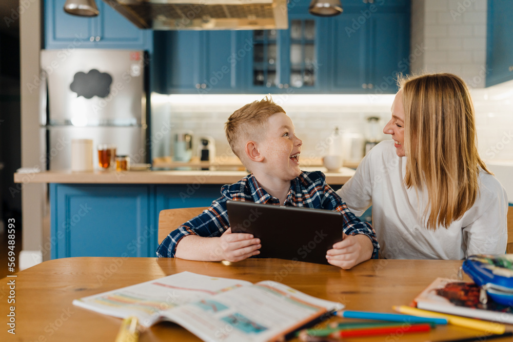 Cheerful mom and son using tablet computer while sitting in kitchen