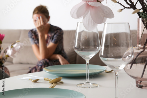 Tired and depressed woman waiting for guests near arranged dinner table. Sad woman waiting alone in the apartment. Exhausted girl waiting for her date. 