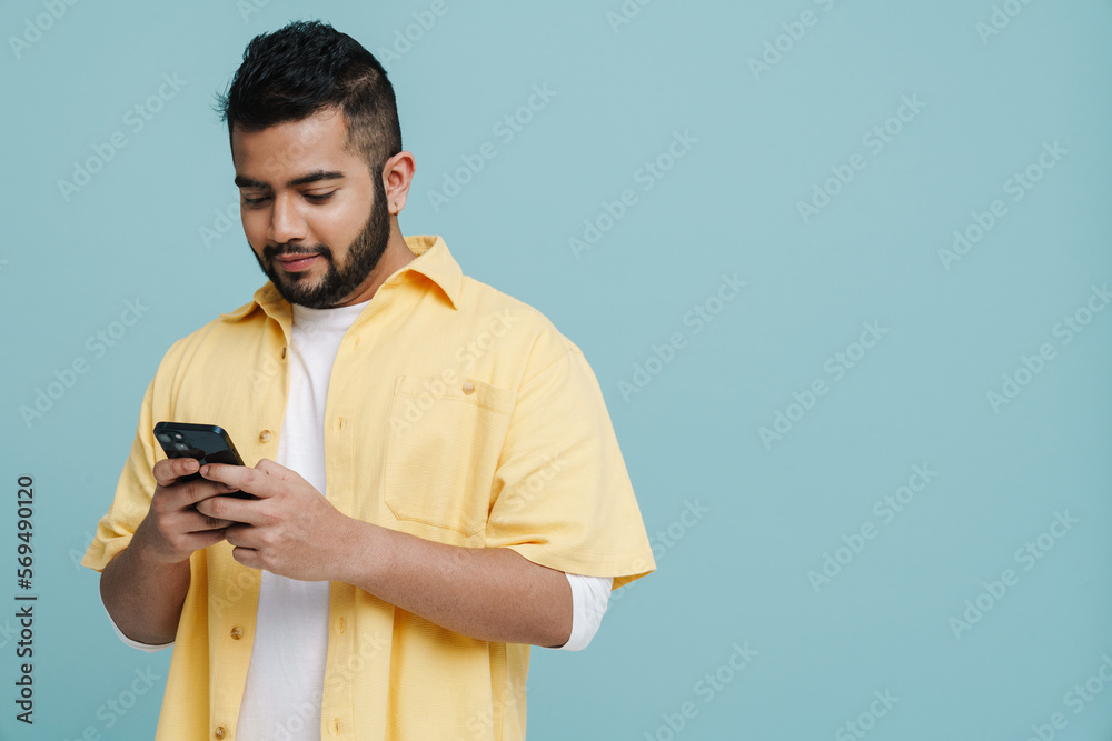 Young indian guy using mobile phone isolated over blue wall Young indian guy using mobile phone isolated over blue wall