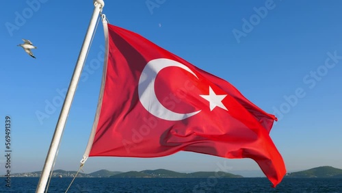 The Turkish flag is flying in the wind, seagulls are soaring in the sky, and the Prince's Islands can be seen in the distance. Ensign at stern of ferry boat sailing from Prince Islands to mainland photo