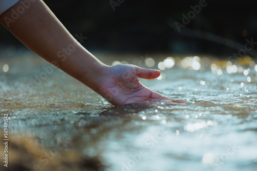 Hand touching the surface of water in the river at the morning time with sunlight. People enjoying with nature and healthy lifestyles concept.