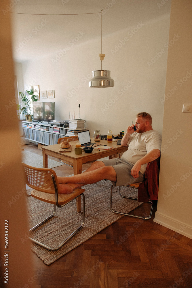 Overweight man talking on smart phone while sitting on chair in living room at home Overweight man talking on smart phone while sitting on chair in living room at home