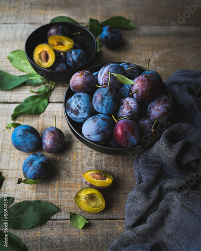 Close up of bowls of fresh picked plums on wooden background.