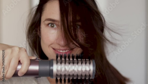 smiling millennial young woman using a modern rotative hair brush for styling.hair dryer and volumizer rotative head slow motion. Thermal and ceramic coating of dryer.tangled hair before after photo