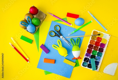 Easter layout on a yellow background, children's crafts, coloring Easter eggs. On the table are multi-colored paints, plasticine. Concept creative, holiday bright easter. Flat lay. 