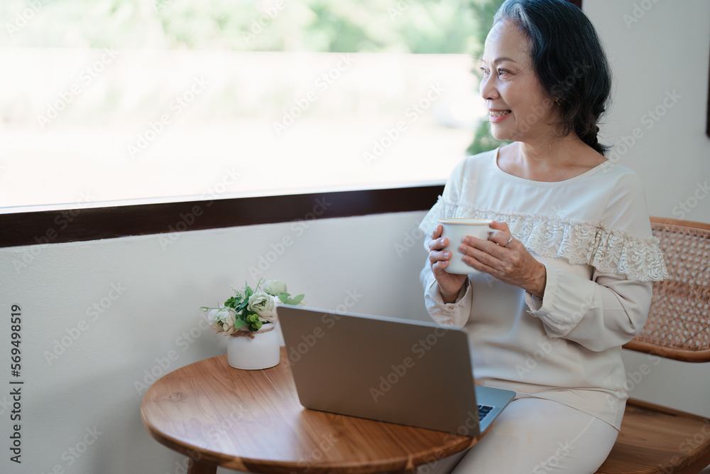 Portrait of an elderly Asian woman in modern pose doing computer work and drinking coffee. Portrait of an elderly Asian woman in modern pose doing computer work and drinking coffee.