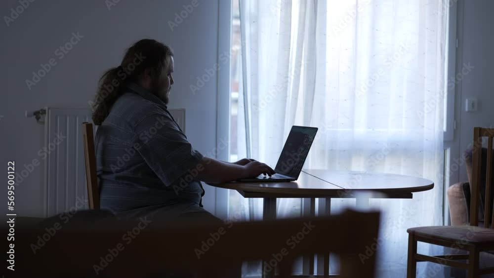 Candid young man working from home in front of laptop computer. Person typing on keyboard using modern technology Candid young man working from home in front of laptop computer. Person typing on keyboard using modern technology