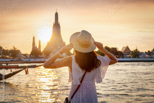 A tourist woman enjoys the view to the famous Wat Arun temple in Bangkok, Thailand, during golden sunset time photo