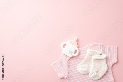 Baby shower concept. Top view photo of pink shirt tiny socks and bottle shaped teether on isolated pastel pink background with copyspace