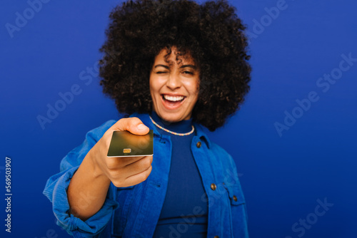 Cheerful young woman holding out her credit card in a studio