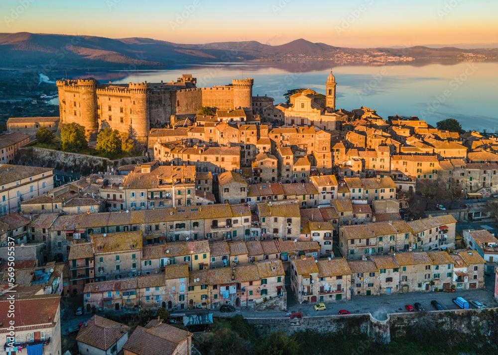 Sunset Panoramic view of the old town of Bracciano perched above the calm waters of Lake Bracciano, near Rome, Italy - Orsini-Odescalchi castle, Duomo and village lit by the golden hour light
