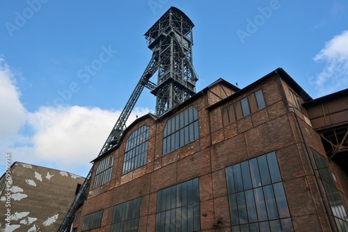 Historic coal mining tower and industrial buildings in Ostrava, Czech Republic. Bottom view of a brick building with tall windows and in the background with a steel mining tower. photo