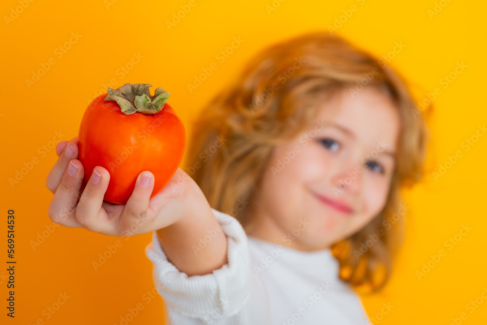 Kid with persimmon in studio. Studio portrait of cute child hold persimmon isolated on yellow background. Kid with persimmon in studio. Studio portrait of cute child hold persimmon isolated on yellow background.