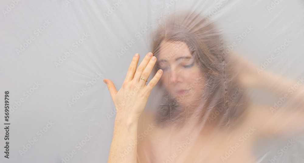 Fototapeta premium blurred, fuzzy image of sensual romantic young naked red hair woman portrait behind plastic film, shows hand with wedding ring, looks like renaissance madonna, looking down
