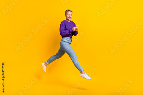 Full body portrait of excited energetic lady jump rush hold use telephone isolated on yellow color background