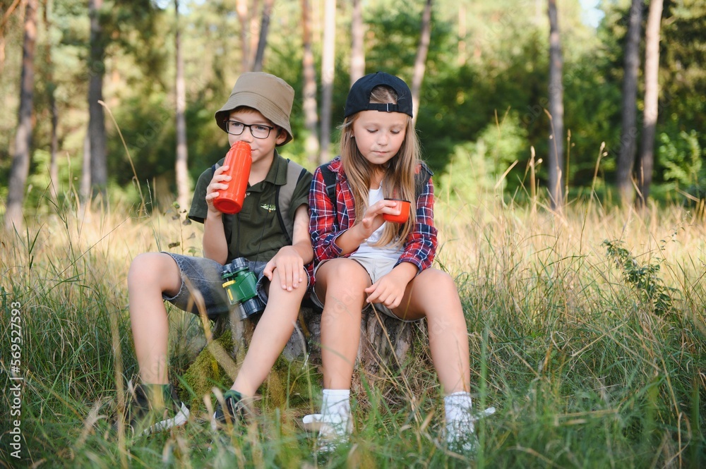 Fototapeta premium Girl and boy scout sitting and drinking hot tea from thermos in the woods