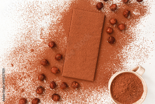 Hazelnuts with a chocolate bar sprinkled with cocoa on a white background