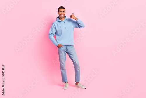 Photo of positive satisfied stylish man wear trendy blue comfort street style outfit thumb up empty space isolated on pink color background