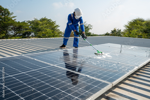 Technician using a mop and water to clean the solar panels that are dirty with dust and birds' droppings to improve the efficiency of solar energy storage.