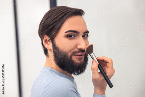 Transgender person applying powder to the face