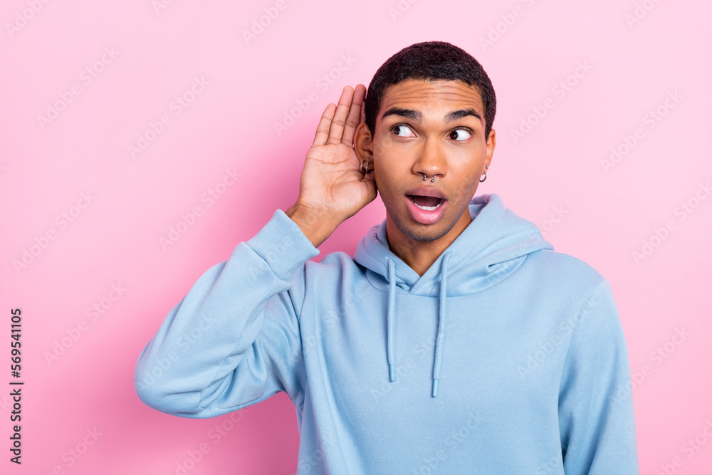 Portrait photo of funny excited young man wear blue sweatshirt earrings listen secret rumor surprised unexpected isolated on pink color background