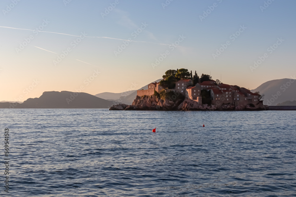 Panoramic sunset view of idyllic island Sveti Stefan in Budva Bay, Adriatic Mediterranean Sea, Montenegro, Europe. Silhouette of Dinaric Alps in back. Summer vacation in exclusive luxury seaside hotel