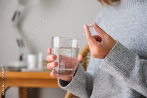 Closeup image of a woman holding white pills and a glass of water photo