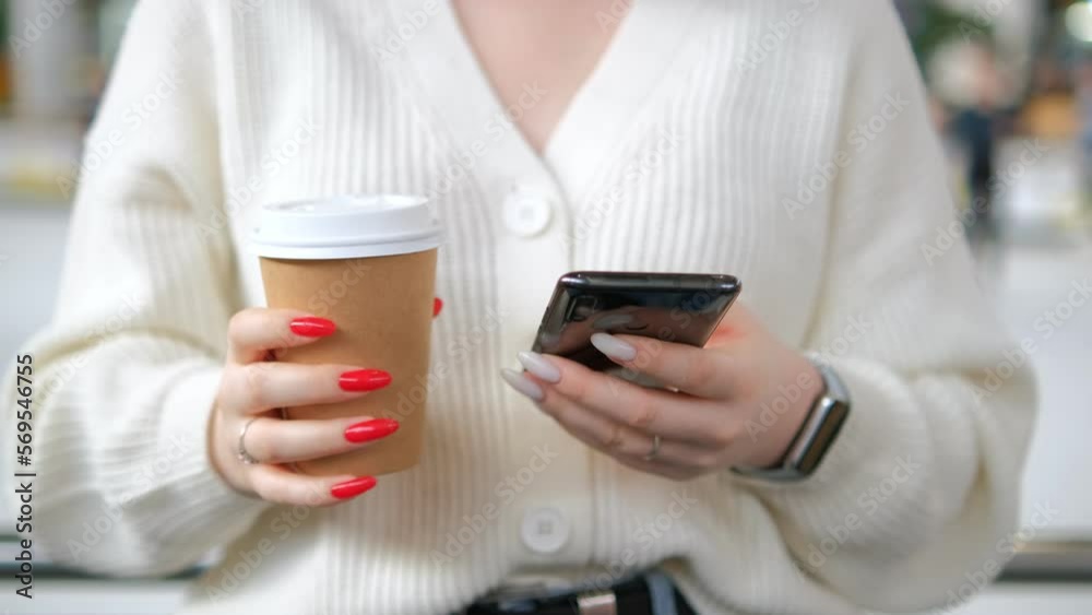 Close up of hands of unrecognizable business woman drinks coffee sitting on a sofa while using a smartphone. Working woman sends text messages from cell phone, working online. 4k video. Close up of hands of unrecognizable business woman drinks coffee sitting on a sofa while using a smartphone. Working woman sends text messages from cell phone, working online. 4k video.