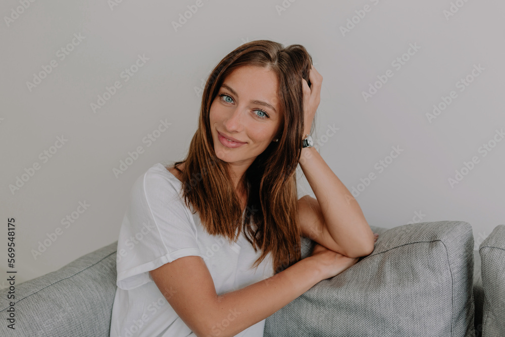 Charming adorable stylish European girl with dark hair and blue eyes posing to camera while sitting on the couch at home with wonderful smile. Charming adorable stylish European girl with dark hair and blue eyes posing to camera while sitting on the couch at home with wonderful smile.