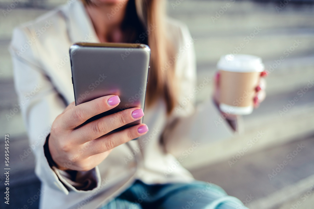 Happy young businesswoman hands typing on phone in city on social media on work break with coffee cup. Happy young businesswoman hands typing on phone in city on social media on work break with coffee cup.
