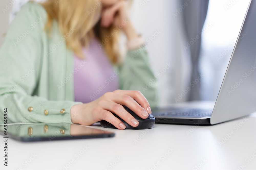 Adult woman working on a computer at home. Unrecognizable white female person clicking with wireless mouse on a laptop - obrazy, fototapety, plakaty 