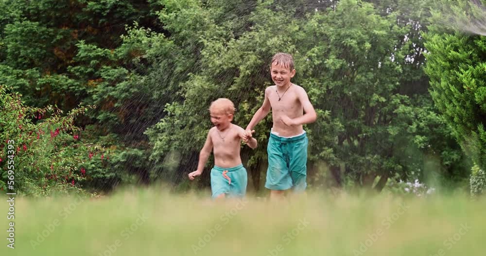 Kids play with water on hot summer day. Children with garden sprinkler having fun. Outdoor fun. Boys run on a field under water drops. Kids play with water on hot summer day. Children with garden sprinkler having fun. Outdoor fun. Boys run on a field under water drops.