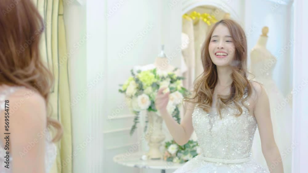 Young asian woman smiling and trying on wedding dress in a shop, asian bride look the mirror for beauty, Young female check beautiful reflection with happy smile for marriage, luxury or fashion Young asian woman smiling and trying on wedding dress in a shop, asian bride look the mirror for beauty, Young female check beautiful reflection with happy smile for marriage, luxury or fashion