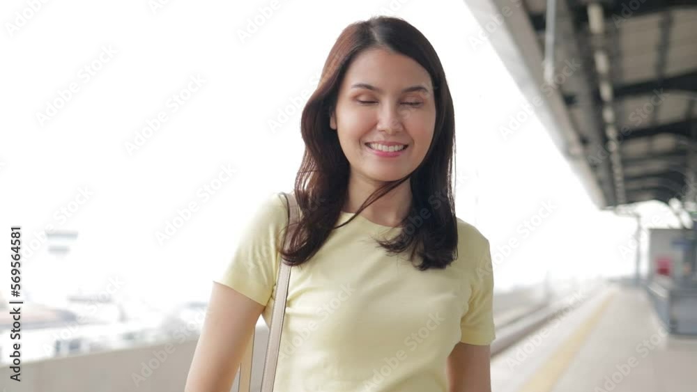 Portrait of beautiful smiling Asian woman standing on platform waiting for electric train in the morning and holding a smartphone. The concept of traffic and capital transportation Portrait of beautiful smiling Asian woman standing on platform waiting for electric train in the morning and holding a smartphone. The concept of traffic and capital transportation