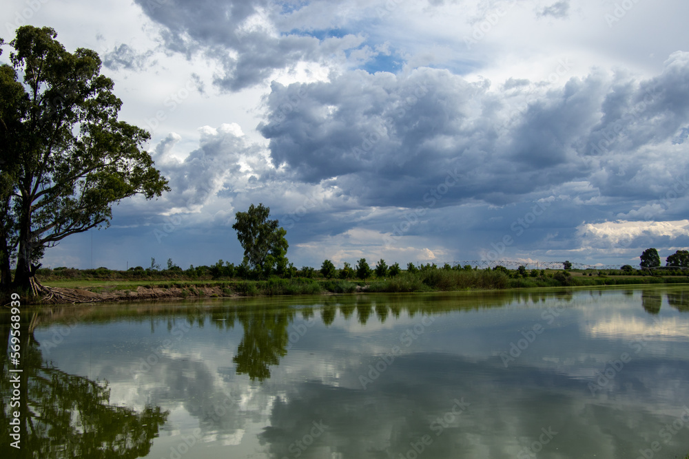 A farm with pivot irrigation next to a river and rain building up