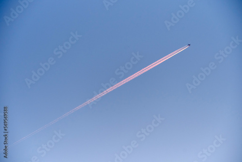 Commercial jet airplane flying high in a clear blue sky leaving a pink contrail trail. Minimalistic aviation background with copy space. Air travel, transportation and climate concept.