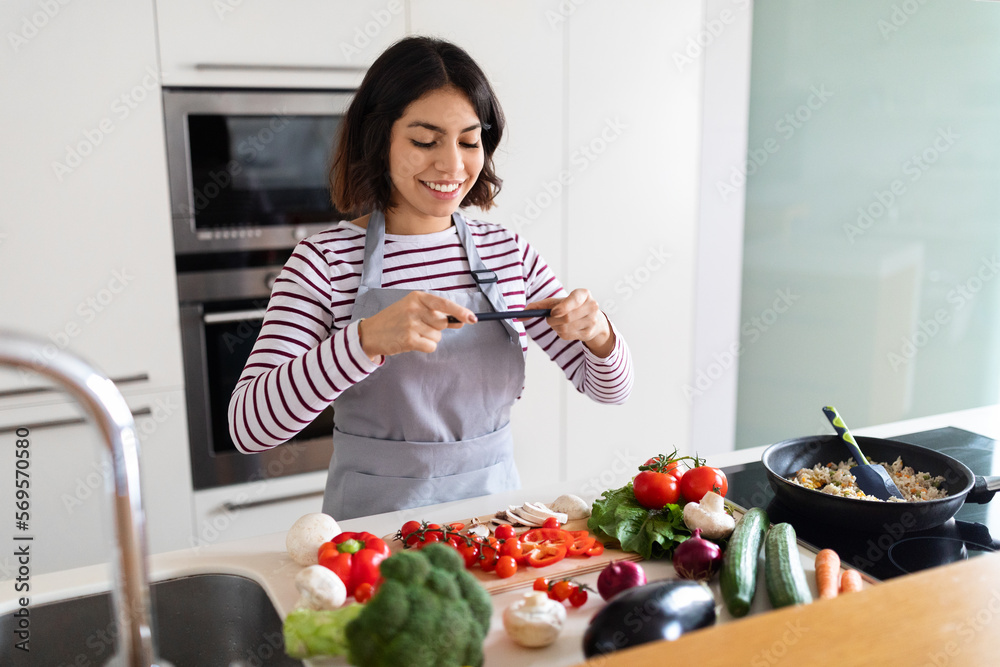 Young woman taking photo with phone while cooking in kitchen