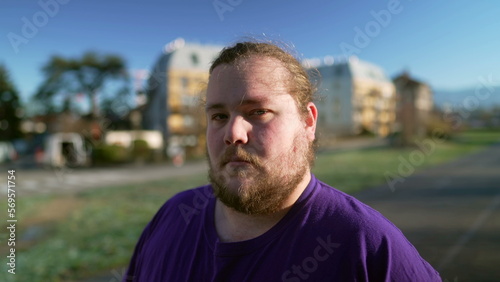 Portrait of a young casual caucasian overweight man standing outside looking at camera with serious expression
