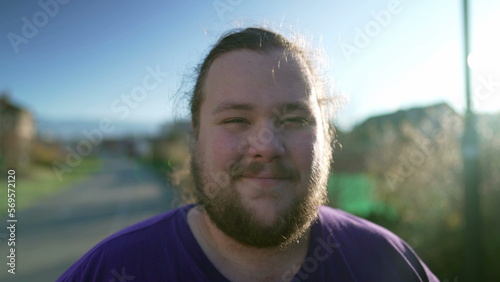 Portrait of a happy overweight young man standing outside looking at camera. One casual male person with beard smiling