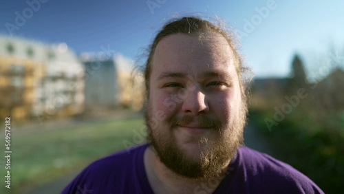 Portrait of a happy overweight young man standing outside looking at camera. One casual male person with beard smiling