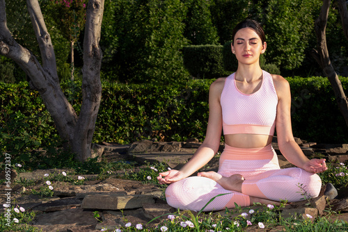 Meditates in nature. A girl is engaged in yoga on the street, in a pink tracksuit does various exercises and yoga poses