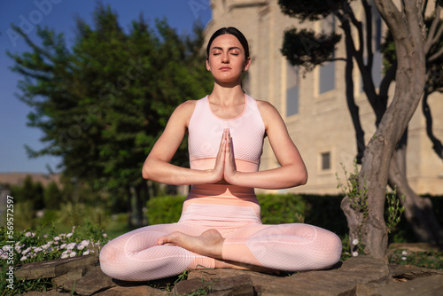 Meditates in nature. A girl is engaged in yoga on the street, in a pink tracksuit does various exercises and yoga poses
